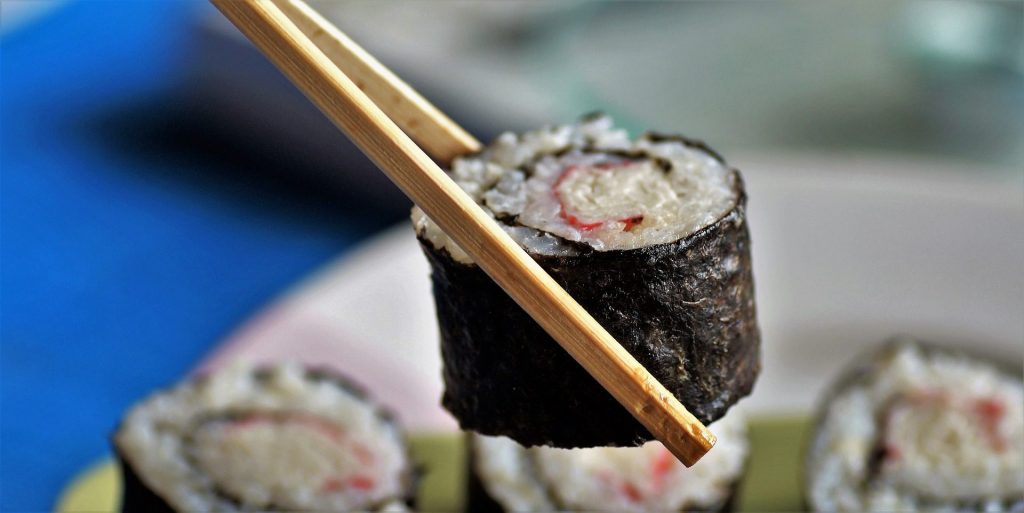 eine Maki Sushi Rolle von zwei Ess-Stäbchen gehalten - dafür muss man die Algen nicht kochen